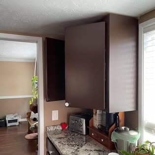 Dark brown kitchen cabinets above a granite countertop with a toaster and small wooden shelf.